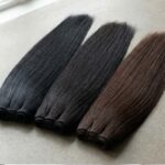 Side-by-side comparison of jet-black Color 1, off-black 1B, and natural color hair bundles showing warm brown undertones in sunlight.