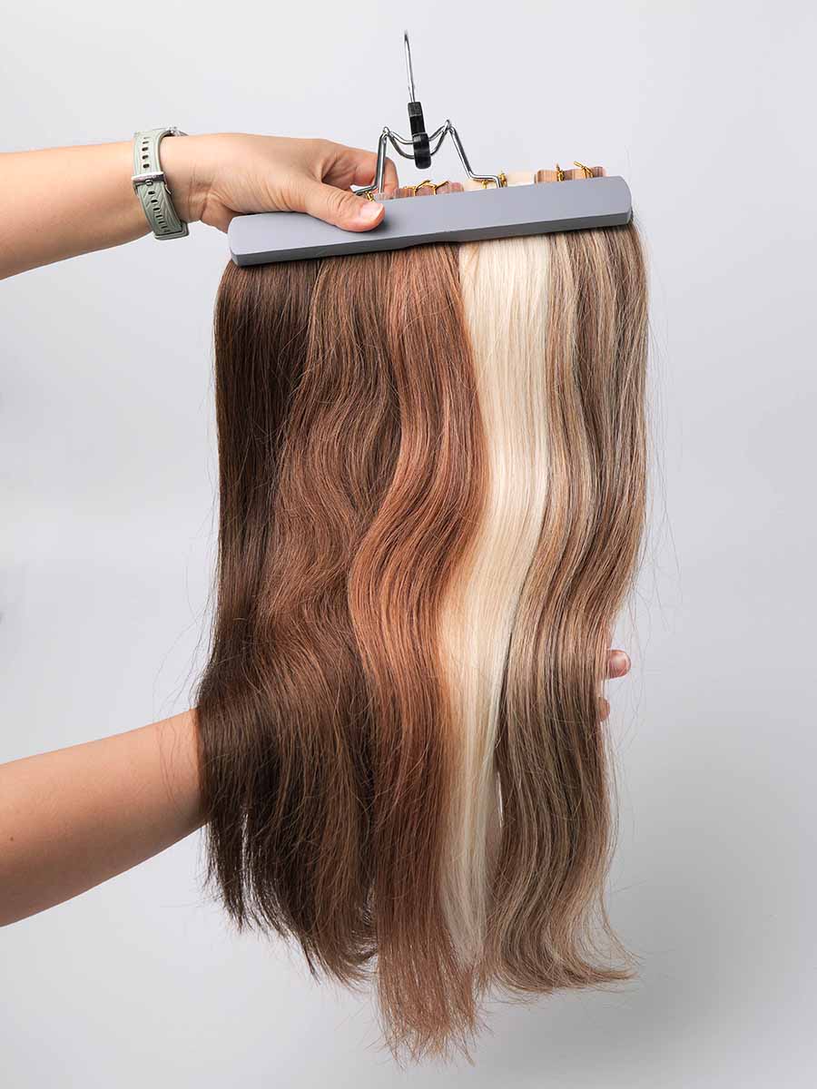 Five bundles of colored straight tape-in extensions held straight by hand, showcasing full length and color variety.