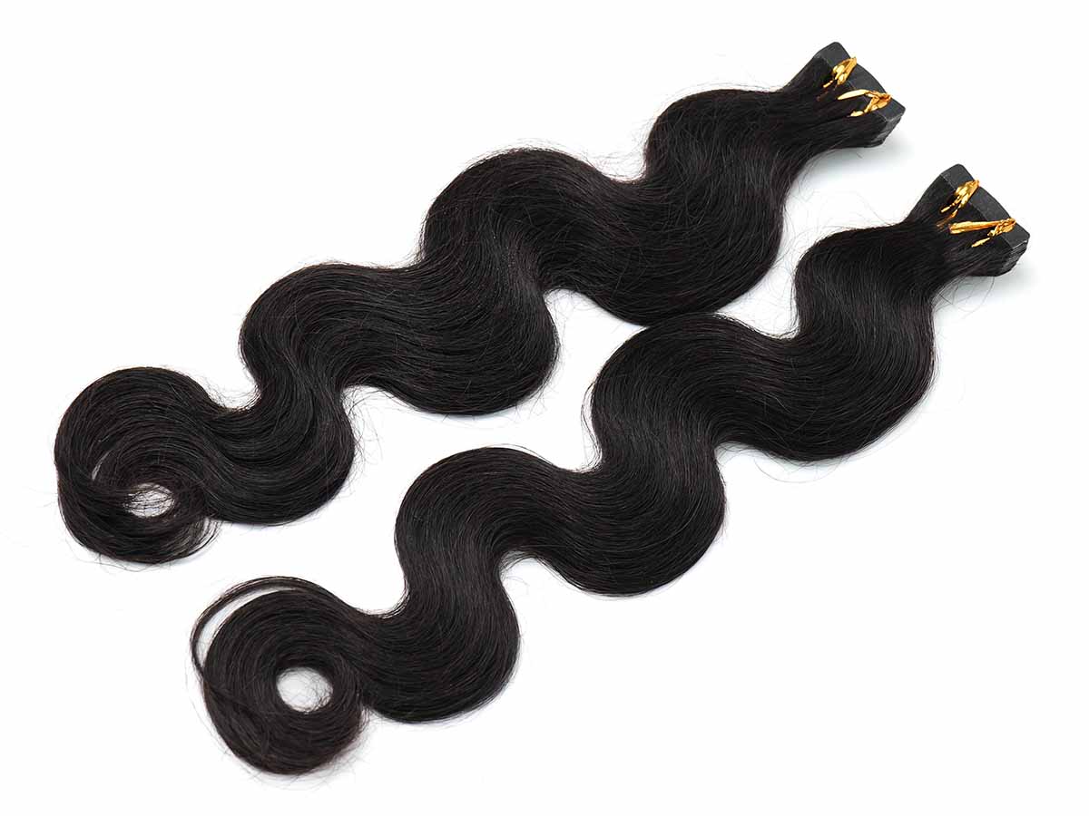 Angled photo showing two full bundles of Black Line body wave tape-in extensions laid out together.