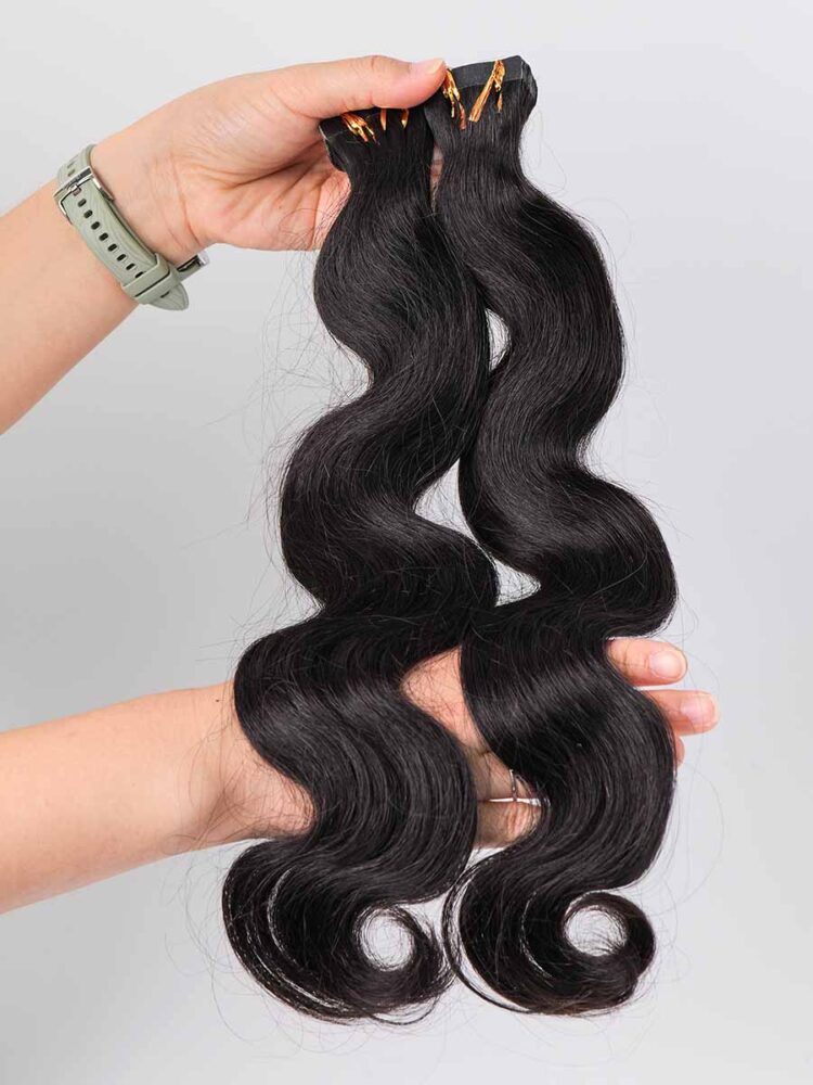 Two sets of body wave tape-in extensions held by hand, showing the wave texture and bundle thickness.