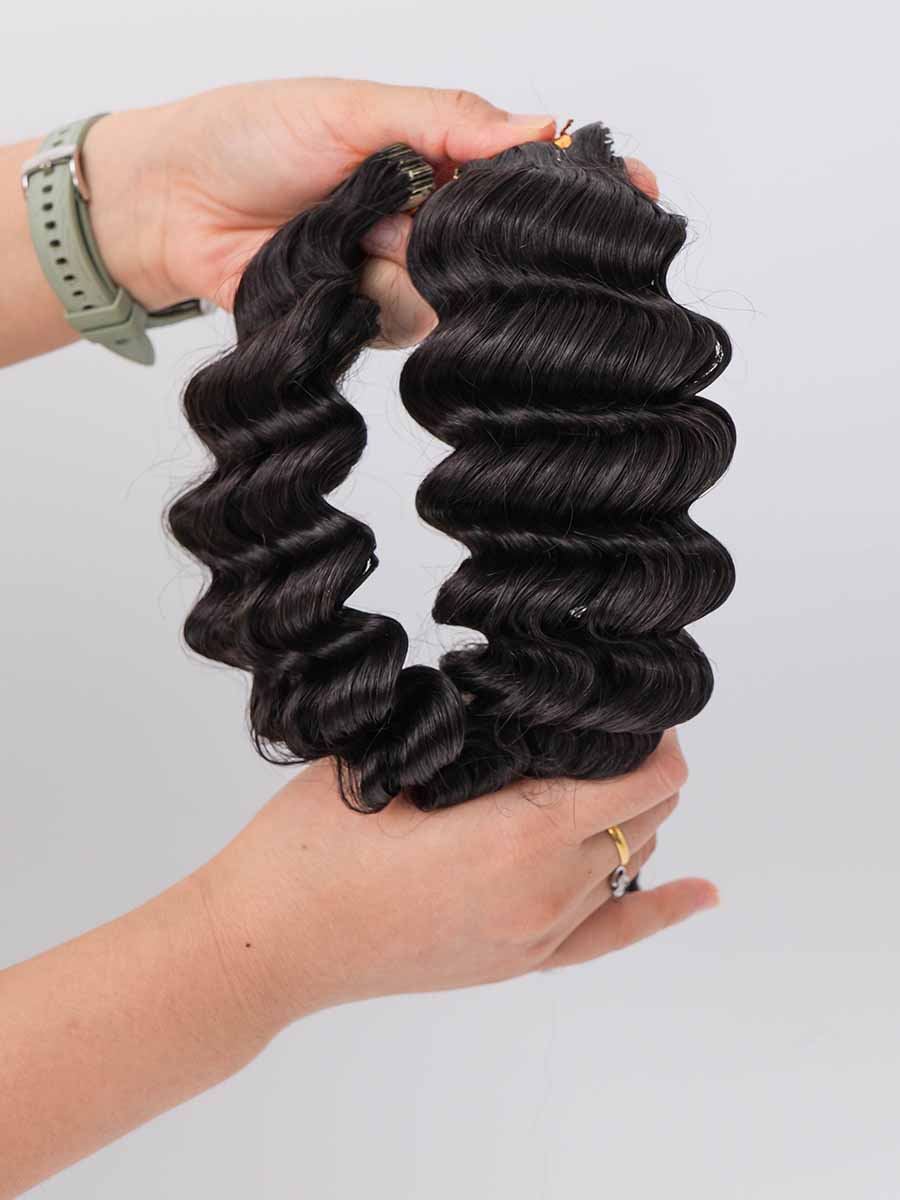 Two sets of deep wave tape-in extensions held in hand, with the hair naturally curved.