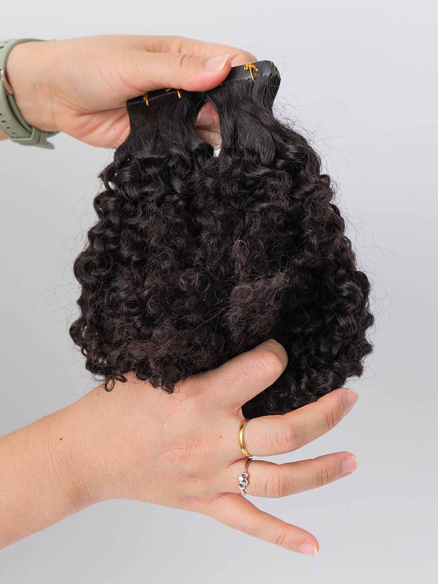 Jerry curl tape-in extensions held in hand with the ends folded upward, showing curl pattern and tip shape.