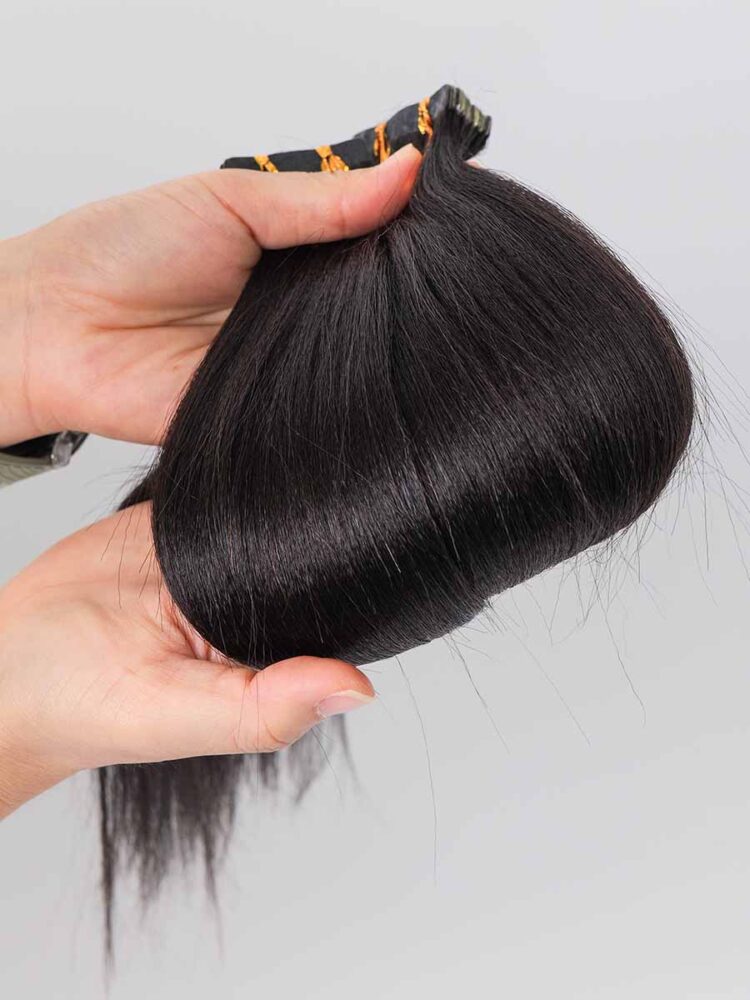 Yaki tape-in extensions held in hand with a visible curve, showing the textured finish of the hair.