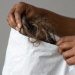A close-up photograph of a pair of hands pulling a dry, tangled mess of frizzy hair from a plastic shipping mailer, illustrating the quality control risks of dropshipping hair extensions.